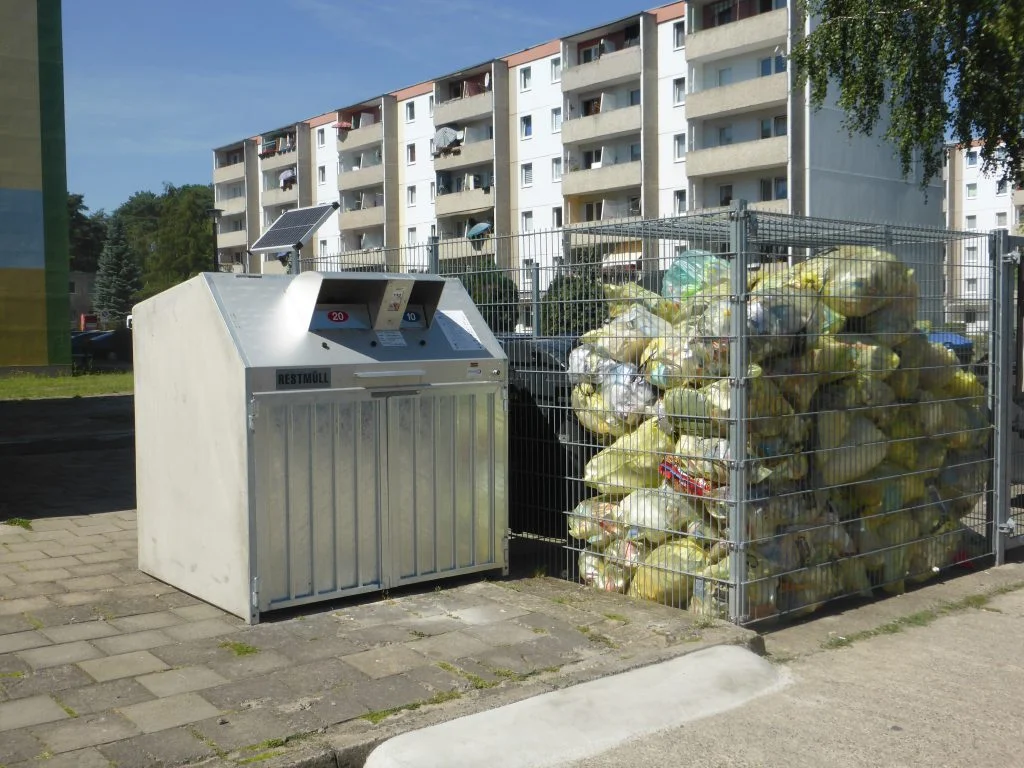 Neuer Restmüll-Sammelbehälter und Sammelstelle für Gelbe Säcke vor Wohnblöcken
