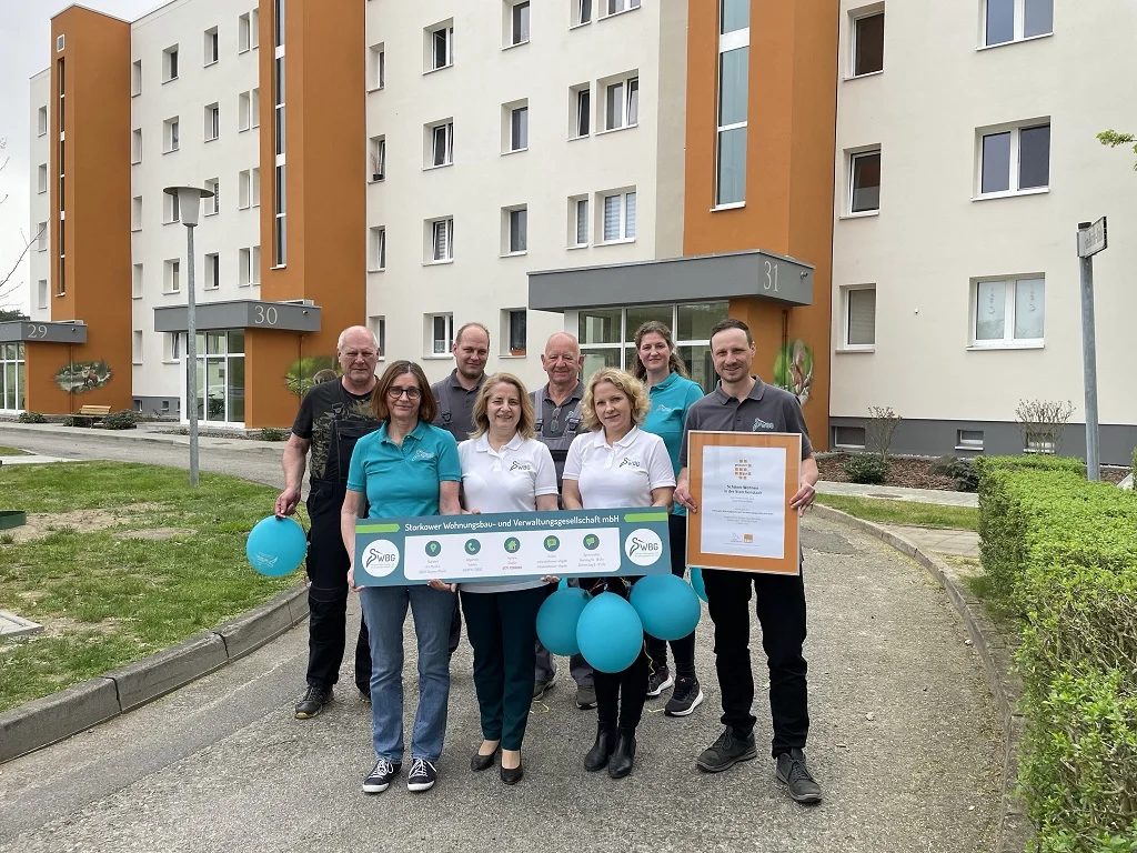 Team der Storkower WBG mit dem Siegel „gewohnt gut“ und Bannern vor den Wohnhäusern